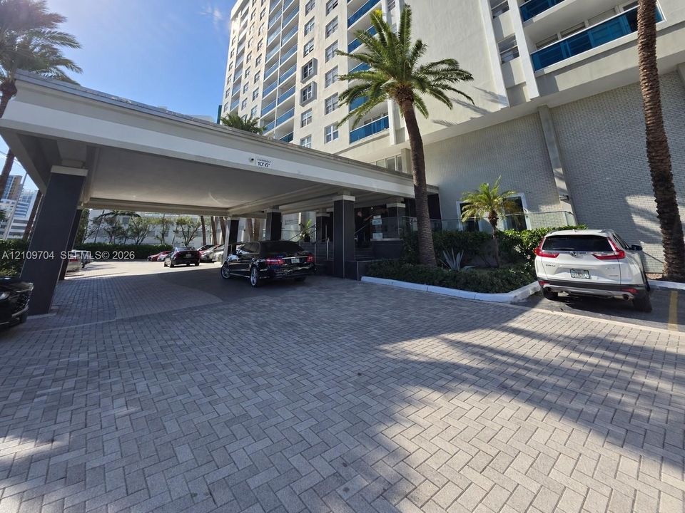 High-rise exterior featuring a paved porte-cochère, covered drop-off area, multi-story facade with glass railings, and mature palm trees
