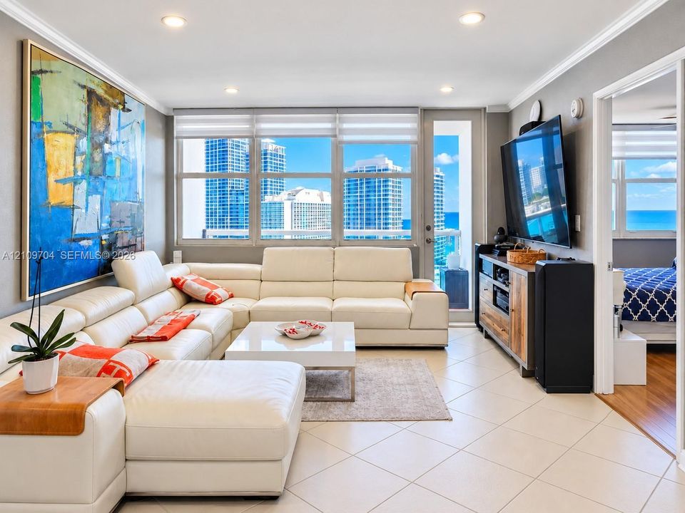 Living area featuring large format tile flooring, recessed ceiling lighting, and floor-to-ceiling windows with panoramic city and coastal scenery