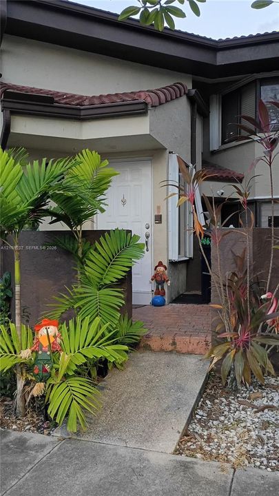 Multi-story residence featuring a stucco facade, brick walkway, and landscaped garden beds with mature palms