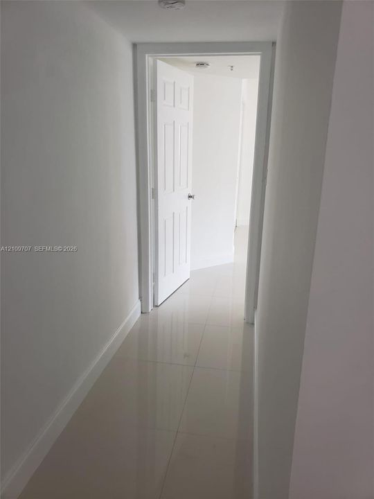 Hallway featuring large-format ceramic tile flooring and a six-panel interior door with brushed metal hardware