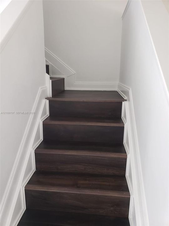 Staircase featuring wood-finish treads and custom white millwork detailing along the stringers