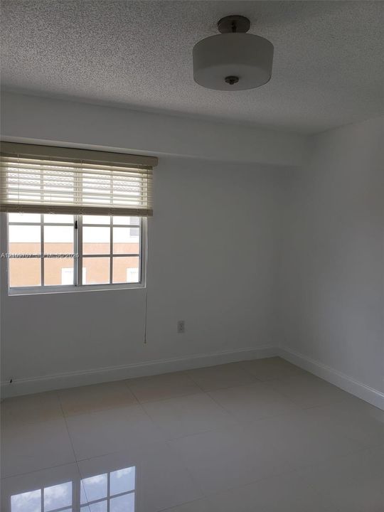 Neutral interior space featuring polished tile flooring, a multi-pane window with installed blinds, and a semi-flush mount drum lighting fixture