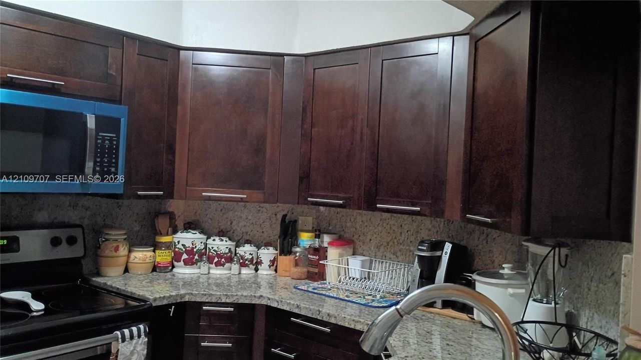 Dark-finish cabinetry with modern hardware, stone-composite countertops, and a stainless steel pull-down kitchen faucet