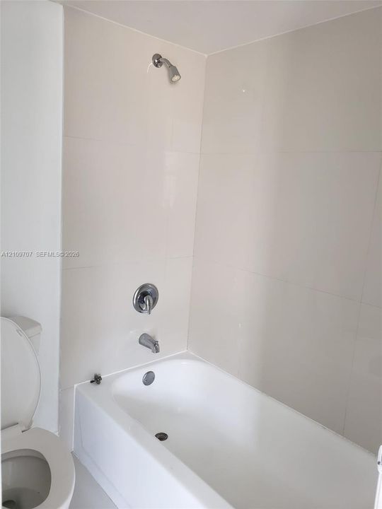 Full-size bathtub with integrated shower, polished chrome single-handle faucet, and floor-to-ceiling tile surround