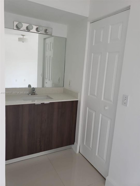 Vanity featuring dark-toned cabinetry, a light-colored solid surface countertop, an integrated rectangular sink, a large wall-mounted mirror, and a four-light fixture
