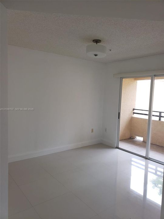 Interior space featuring large-format tile flooring, a semi-flush mount drum ceiling light fixture, and floor-to-ceiling sliding glass doors opening to a private balcony with metal railing
