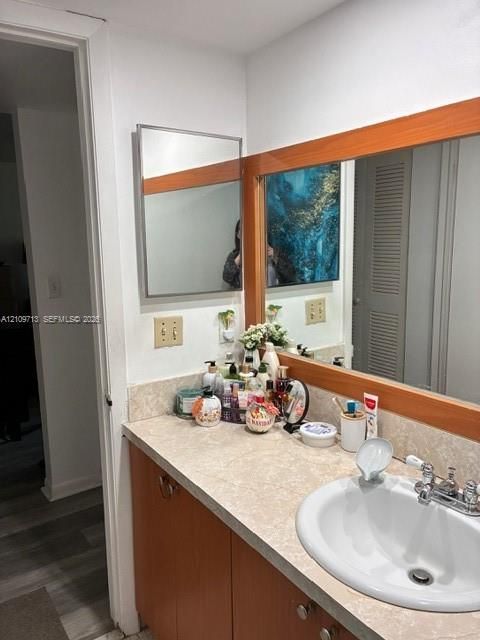 Vanity featuring wood-finish cabinetry, a stone-pattern countertop, an integrated drop-in sink with a chrome dual-handle faucet, and an expansive wall-mounted mirror with wood trim