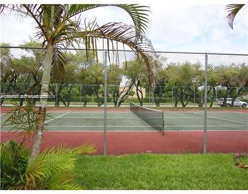 Tennis court featuring a multi-colored hard surface, perimeter chain-link fencing, and native palm landscaping