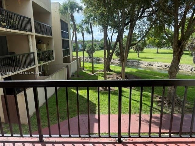 Multi-level balcony featuring black metal railings, overlooking a canal, manicured green space, and mature palms