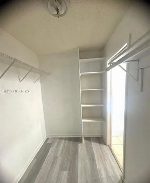 Walk-in closet featuring wood-finish flooring, built-in shelving, and dual wire shelving rods