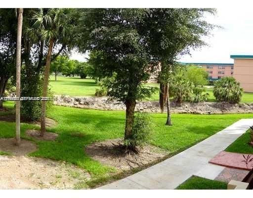Expansive landscaped grounds featuring mature palm and deciduous trees, a stone retaining wall, and concrete paved walkways