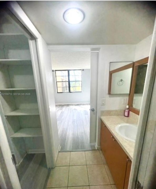 Bathroom featuring a vanity with a neutral-toned countertop and integrated sink, a recessed linen storage cabinet with fixed shelving, ceramic tile flooring, and a wall-mounted mirror