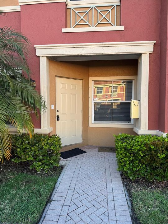 Stucco exterior entrance featuring a paver walkway, decorative railings, and molded trim accents