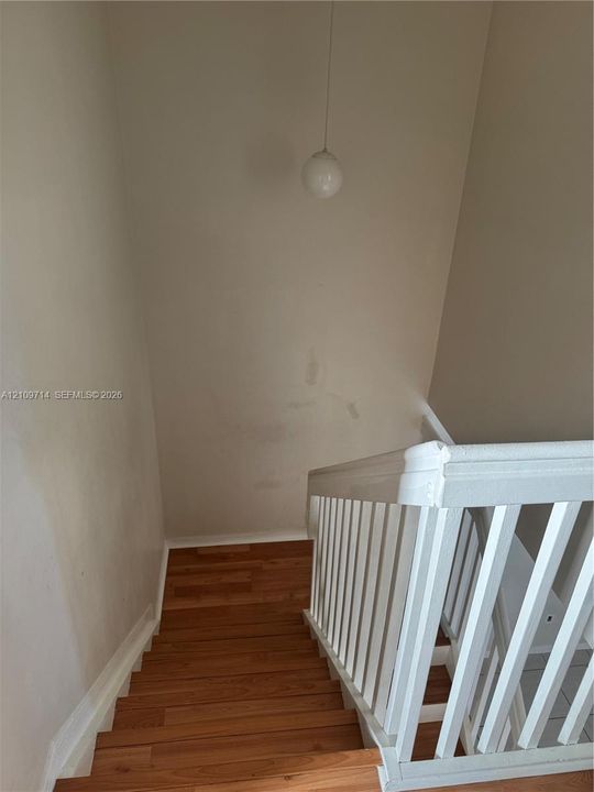 Staircase featuring wood-finish flooring, white painted balustrade with a square newel post, and a spherical pendant light fixture