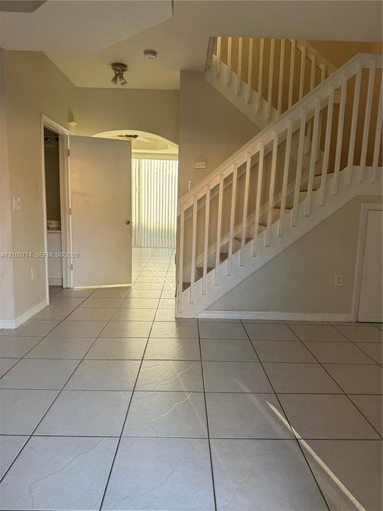 Interior featuring light-toned tile flooring, a white staircase with a matching wooden handrail and balusters, and a recessed archway