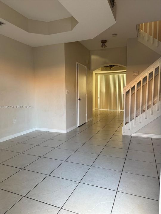 Neutral ceramic tile flooring, architectural tray ceiling, and a wooden staircase with painted white balusters