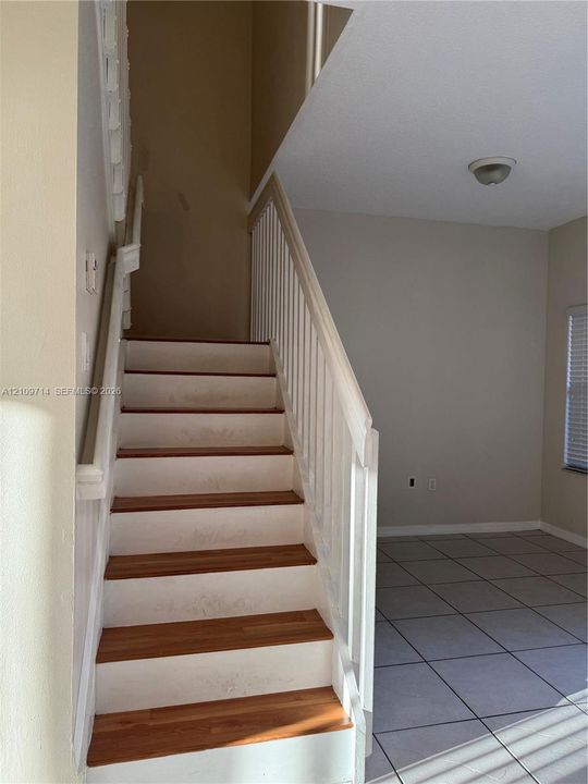Staircase featuring wood-finish treads, white risers, and a painted white balustrade with a wooden handrail, complemented by neutral tile flooring