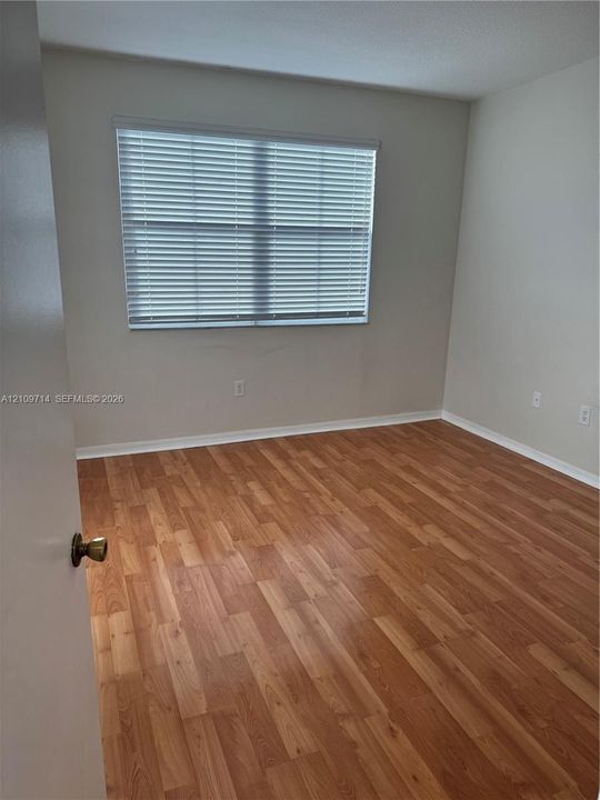 Room featuring wood-finish flooring, neutral wall paint, and a single-pane window with horizontal blinds