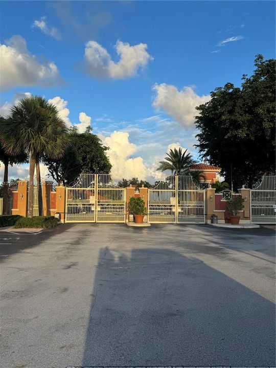 Gated entrance featuring decorative stucco pillars and white metal fencing
