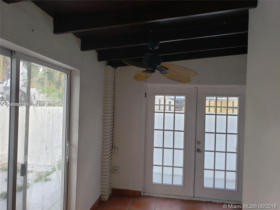 Exposed dark-finish ceiling beams, ceramic tile flooring, brick-style accent column, multi-pane glass French doors, and sliding glass panel door