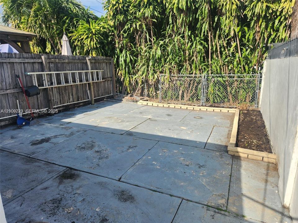 Paved concrete patio featuring a tiered wood planter box, a chain-link rear fence, and a wooden perimeter fence