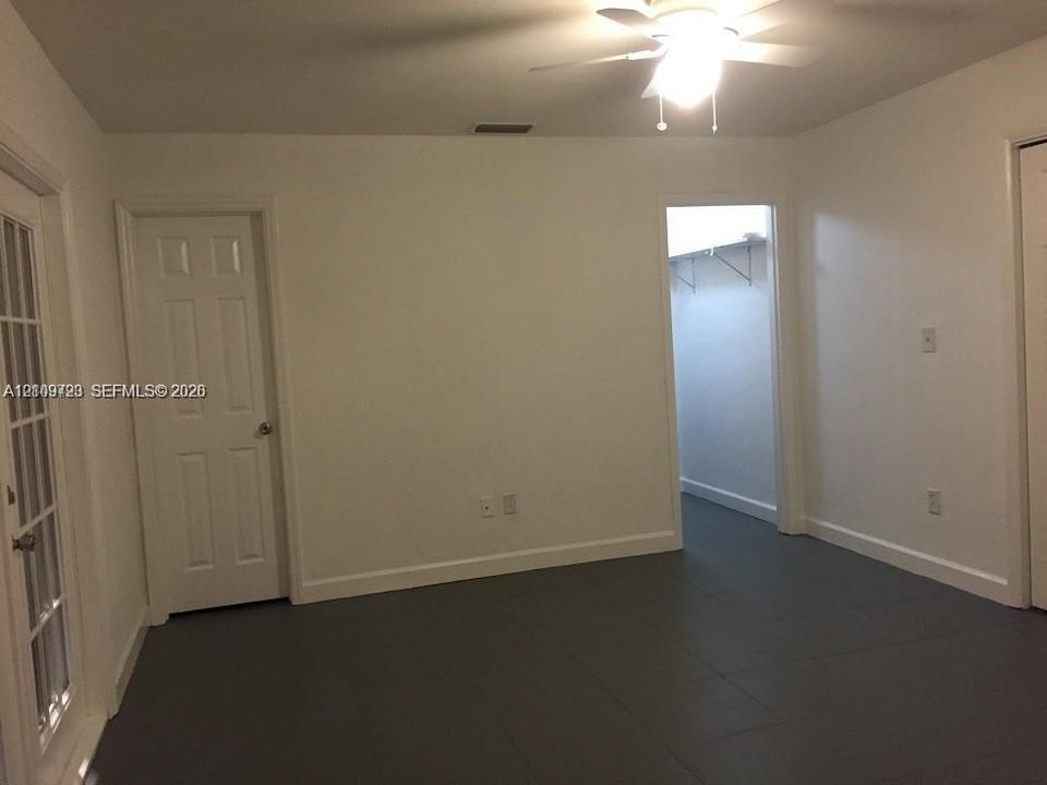 Room featuring large-format tile flooring, a multi-pane French door, a ceiling fan with integrated lighting, and multiple interior doorways