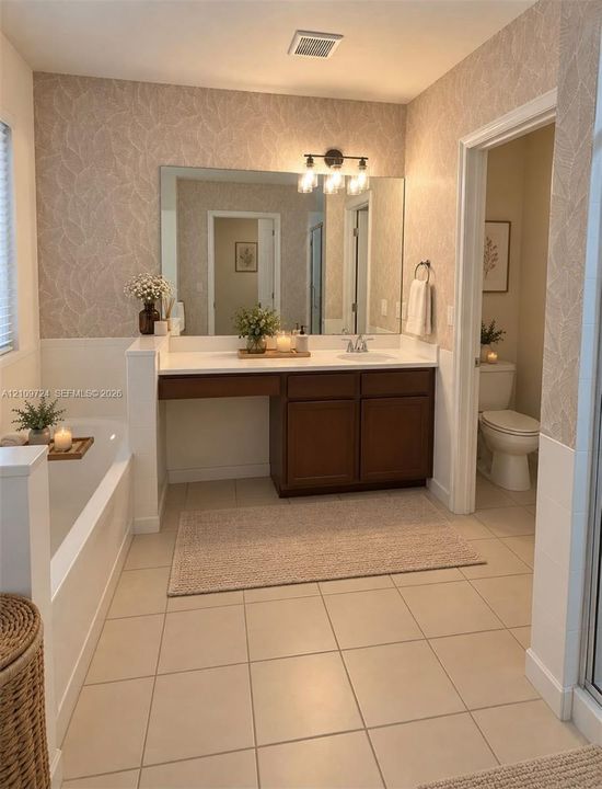 Bathroom featuring a wood-finish vanity with a white countertop, large wall-mounted mirror, integrated soaking tub with a white tile surround, three-light vanity fixture, and neutral ceramic tile flooring
