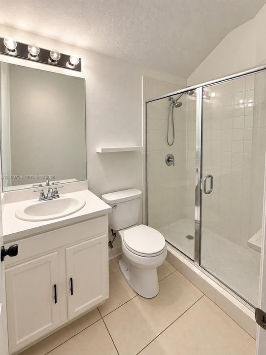 Bathroom featuring a white vanity cabinet with a solid surface countertop, an undermount oval sink, chrome fixtures, and a walk-in tiled shower with a glass enclosure