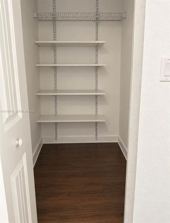 Storage closet featuring wood-finish flooring, white walls, and a multi-tier adjustable shelving system with a wire rack