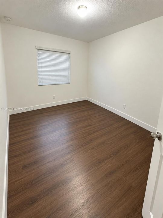Interior space featuring wood-finish flooring, white walls, and a single window with installed blinds