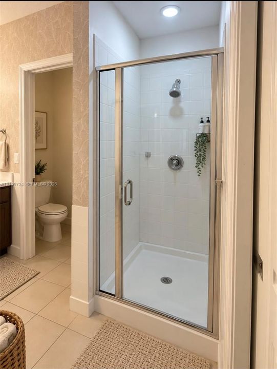 Shower stall featuring a glass door with a polished chrome frame, white tiled walls, and a recessed ceiling light