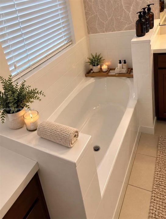 Oval soaking tub with a white tile surround, horizontal window blinds, and tile flooring