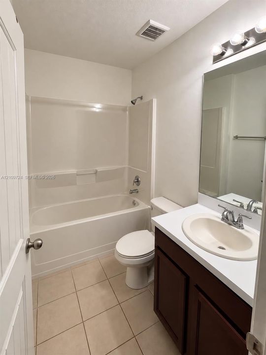 Bathroom featuring a vanity with a white countertop and oval sink, tile flooring, and a shower-tub combination with a wall-mounted fixture