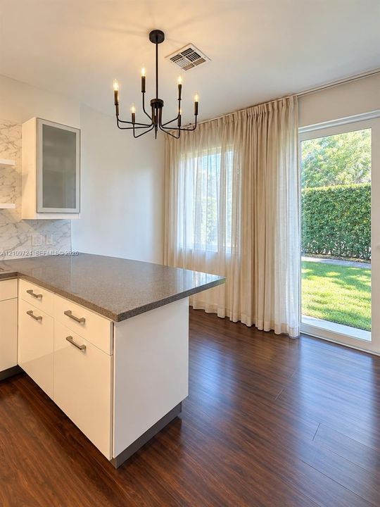 Kitchen featuring a peninsula with stone-finish countertop, white cabinetry with glass-paneled upper storage, wood-finish flooring, and a modern six-light chandelier