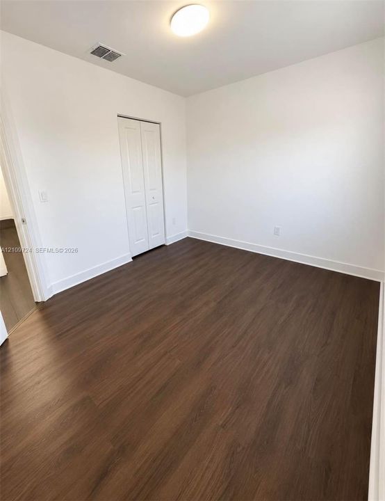 Interior room featuring wood-finish flooring, white walls, and a white bi-fold closet door