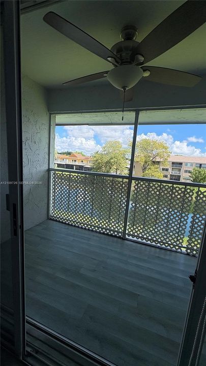 Screened-in balcony featuring wood-finish flooring, a ceiling fan with integrated light fixture, and decorative lattice railing