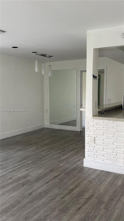 Wood-finish flooring, white painted brick accent wall, built-in floor-to-ceiling mirror, and three-pendant overhead lighting fixture