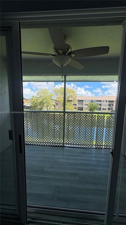 Screened-in balcony featuring wood-finish flooring, a ceiling fan with integrated lighting, and decorative latticework railing