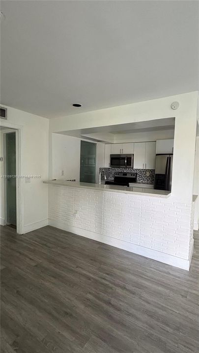 Kitchen featuring white cabinetry, stainless steel appliances, a stone-surfaced peninsula with a white brick facade, and wood-finish flooring