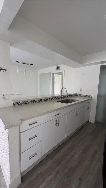 Kitchen featuring white shaker-style cabinetry, quartz countertops, stainless steel undermount sink, multi-tonal mosaic tile backsplash, and wood-finish flooring