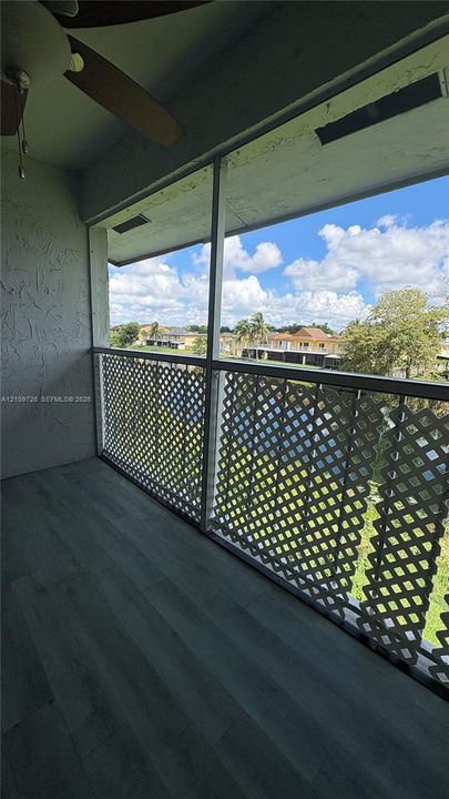 Screened-in balcony with wood-finish flooring, lattice railing, and a ceiling fan