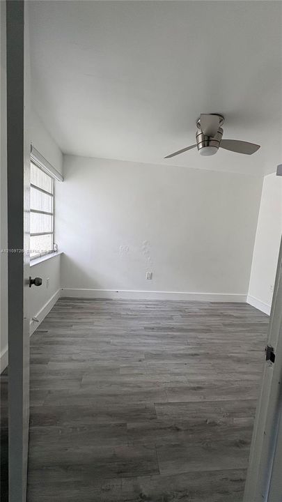 Interior room featuring wood-finish flooring, a multi-pane window, and a central ceiling fan with an integrated light fixture