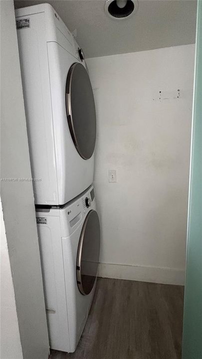 Stacked white front-load washer and dryer unit with metallic-finish door rims and wood-finish flooring