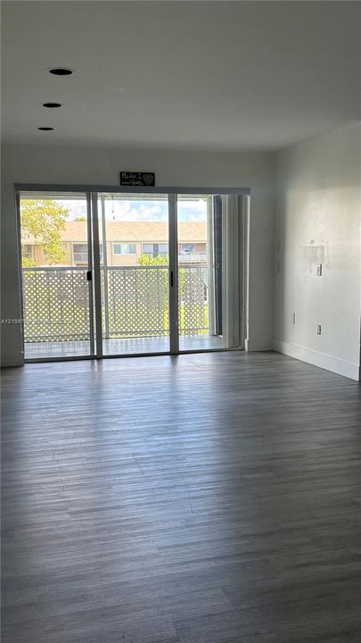 Interior space featuring wood-finish flooring, recessed ceiling lighting, and floor-to-ceiling sliding glass doors opening to a private balcony with lattice railing