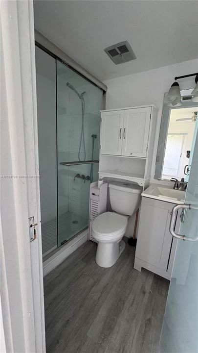 Bathroom featuring a glass-enclosed shower, single-basin vanity with a neutral countertop, wood-finish flooring, and white cabinetry