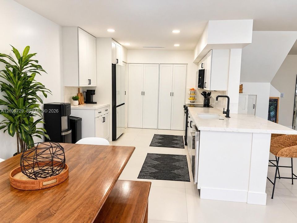 Kitchen featuring white cabinetry, solid-surface countertops, center island with undermount sink, matte black hardware, and recessed ceiling lighting