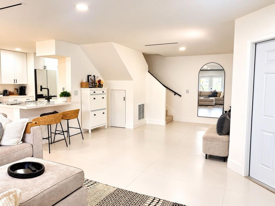 Open-concept interior featuring large-format tile flooring, recessed lighting, breakfast bar with quartz countertop, and arched wall mirror