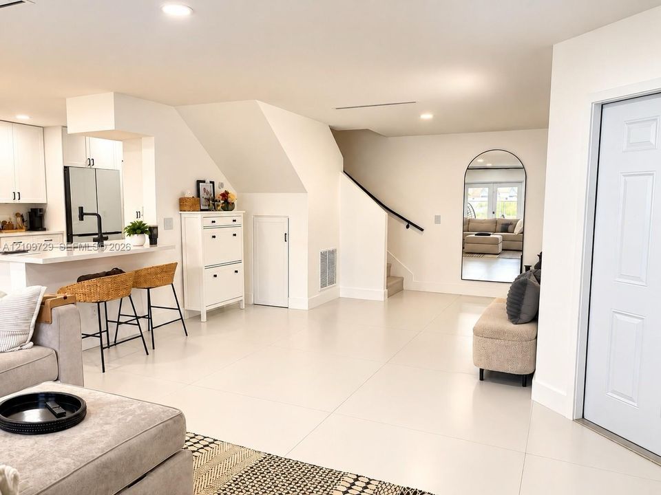 Open interior featuring large-format tile flooring, recessed lighting, kitchen with peninsula, and stairway with a matte black handrail