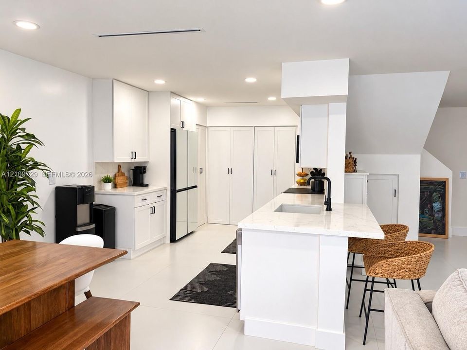 Kitchen featuring white shaker-style cabinetry, quartz countertops, a central island with a built-in sink, matte black hardware, and recessed ceiling lighting