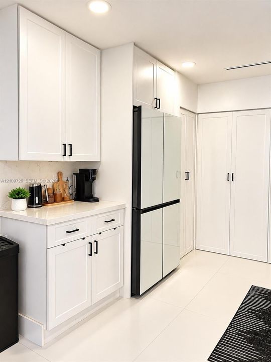 White shaker-style cabinetry with matte black hardware, stone-surface countertops, floor-to-ceiling pantry storage, and polished tile flooring